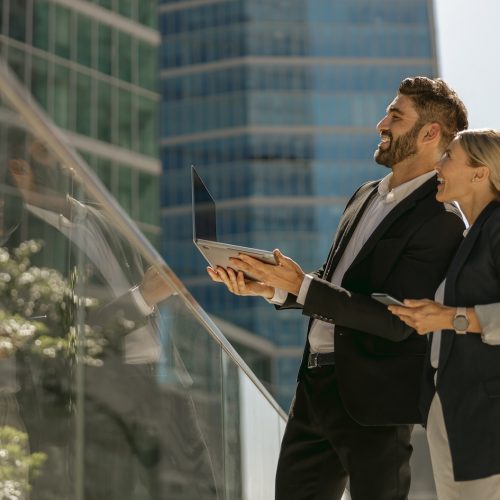 Two business colleagues working on project while standing outdoors on skyscrapers background Business colleagues working on project while standing outdoors on skyscrapers background